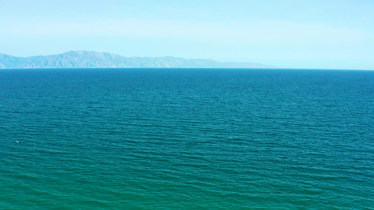 Mid-clip frame showing rippled blue-green water, distant mountainous coastline, and clear sky near El Sargento La Ventana, Mexico, with no visible people.