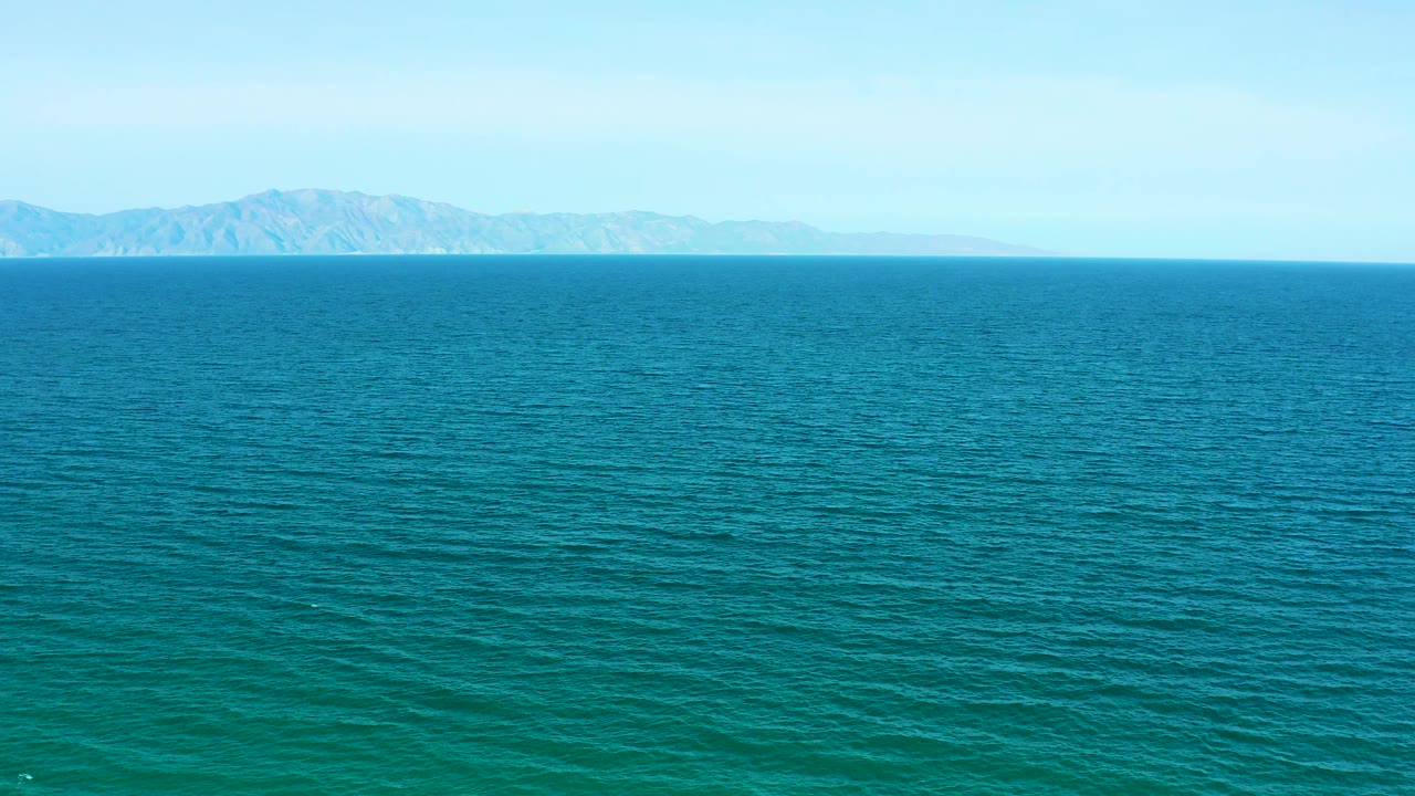 At two seconds, the distant mountainous shoreline remains small above the blue ocean, with pale clear sky overhead and no visible people or boats.