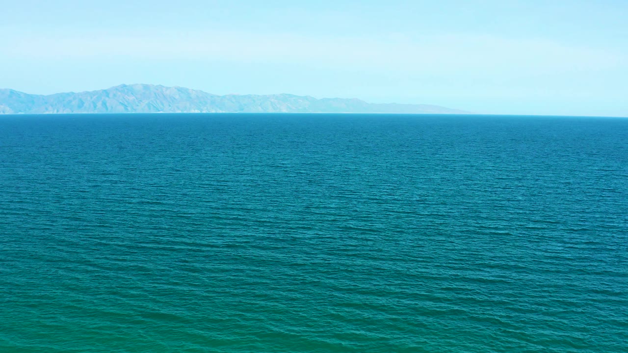 At three seconds, a broad stretch of blue sea leads to a low hazy landmass in the distance near El Sargento La Ventana, with no visible people.