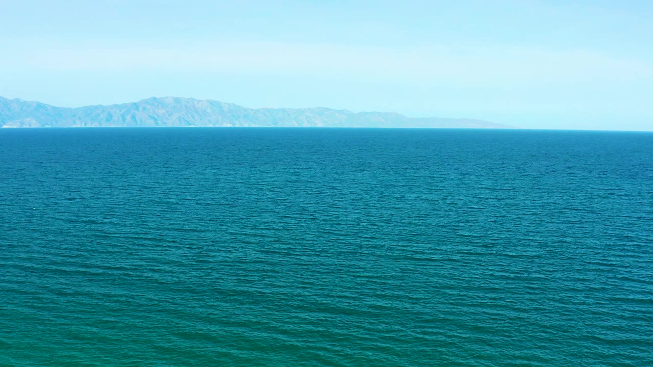 Wide view of teal ocean off El Sargento La Ventana, Mexico, with faint mountains across the horizon, pale blue sky, and no visible people.