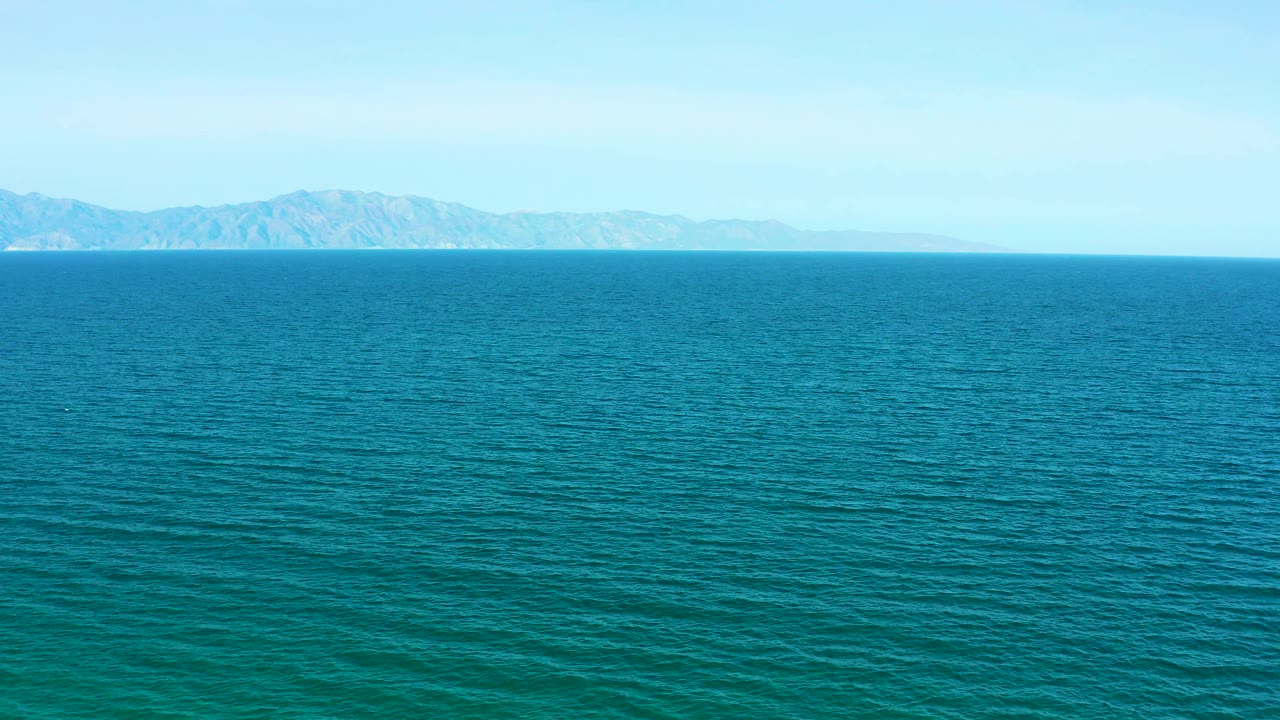 Open blue-green water off El Sargento La Ventana, Mexico, stretches toward a thin mountain horizon under clear daylight, with no visible people.
