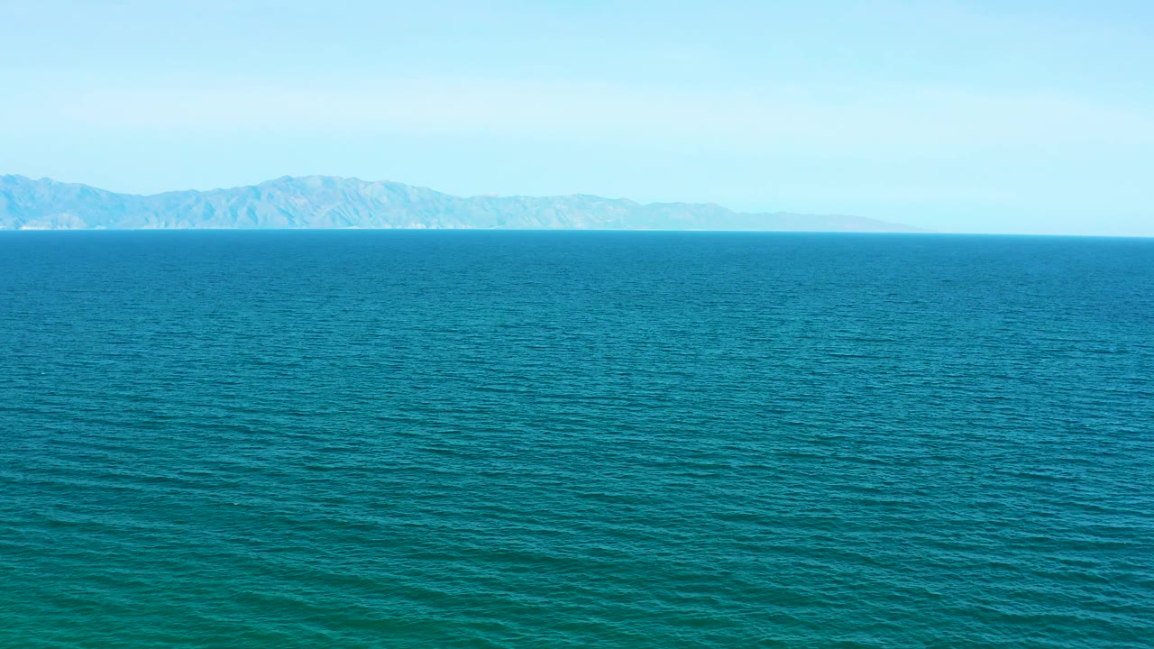 A broad sea surface fills the frame near El Sargento La Ventana, Mexico, with distant landforms softened by haze and no visible people.