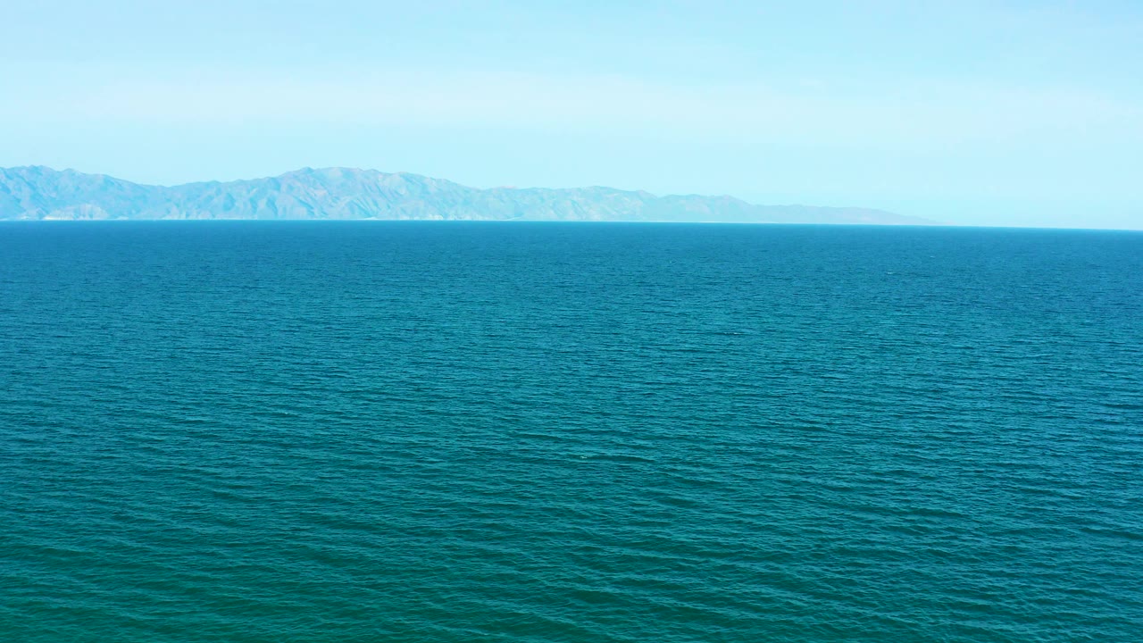 Blue ocean with distant mountain coastline under pale sky