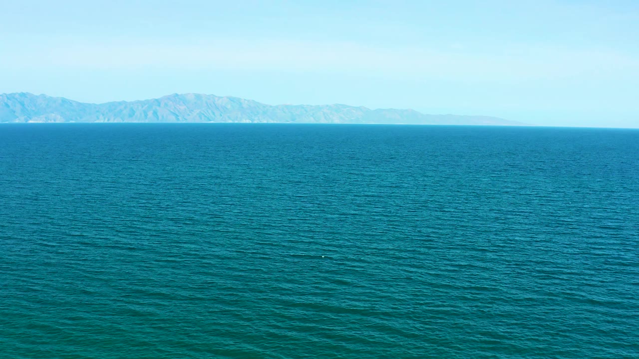 The frame keeps the rugged distant mountains across the upper background while textured ocean fills most of the view, with no visible people or vessels.