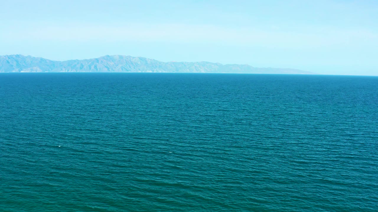 A wide El Sargento La Ventana ocean frame shows a pale mountain coast stretching across the background and empty blue water across the foreground, no visible people.