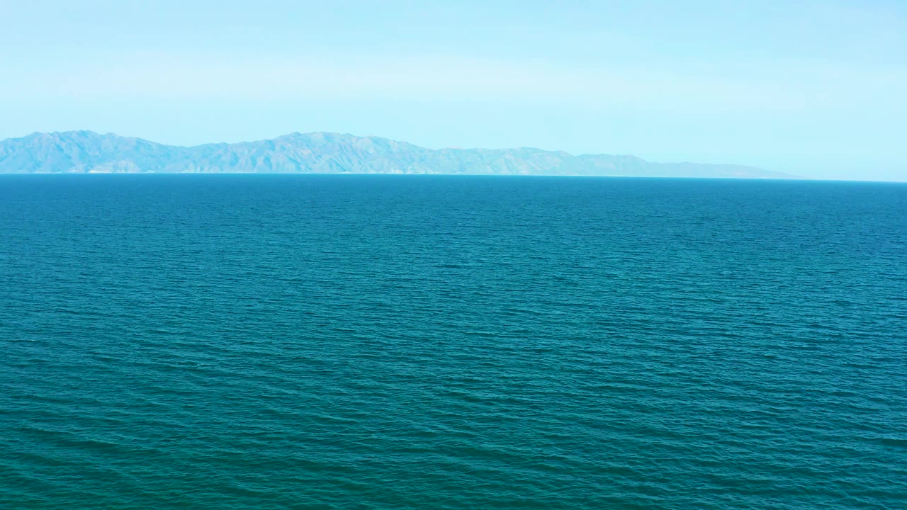 Open turquoise water fills most of the frame, with hazy mountains across the horizon in El Sargento La Ventana, Mexico, and no visible people.