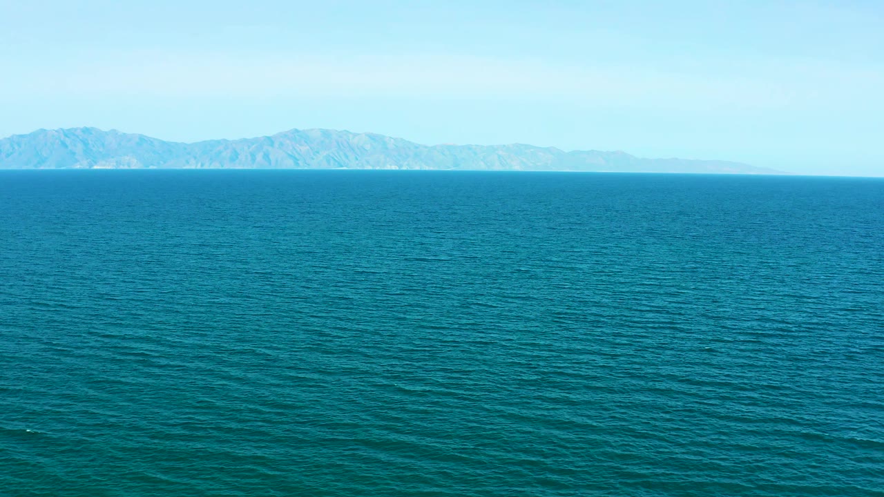 Calm blue ocean surface stretches toward a long mountain horizon in El Sargento La Ventana, Mexico, with no visible people or boats.