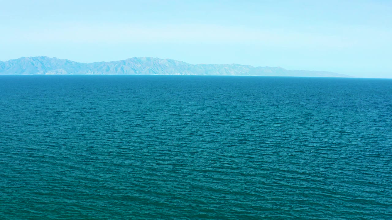 A wide sea surface sits below low distant mountains and bright blue sky in El Sargento La Ventana, Mexico, with no visible people.
