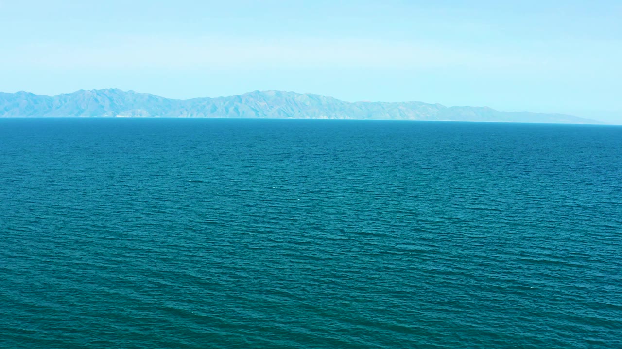 Mid-clip frame from El Sargento La Ventana shows expansive blue-green sea, a thin distant land strip, mountain ridges, clean daylight, and no visible people.