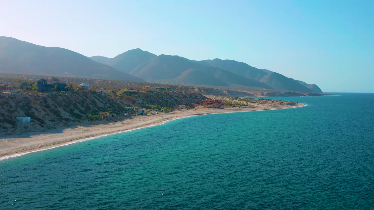 Coastal bluff and beach beside turquoise sea with mountains behind