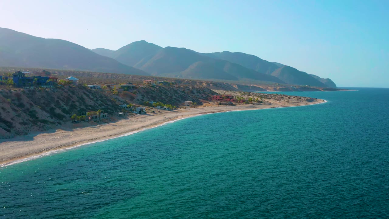 Elevated coastline view with turquoise water, beach, bluffs, and mountains.