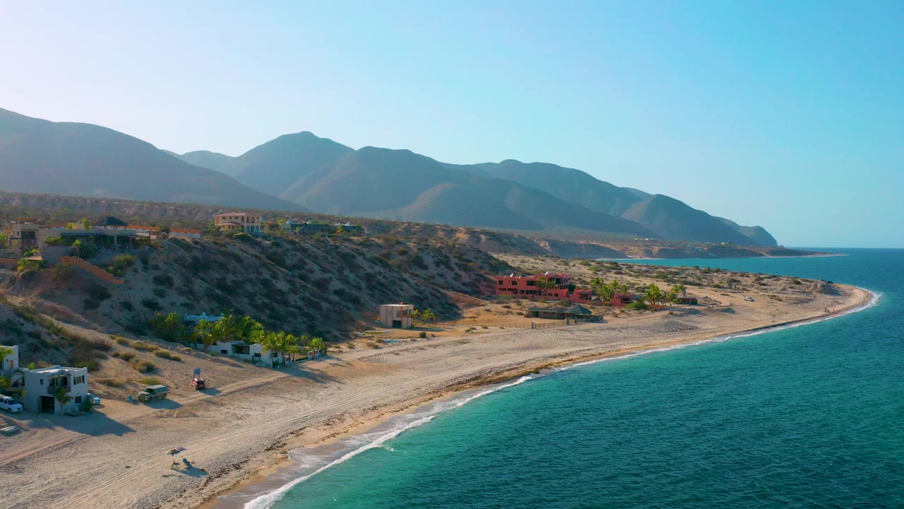 Coastal aerial with turquoise water, sandy beach, palms, and hillside