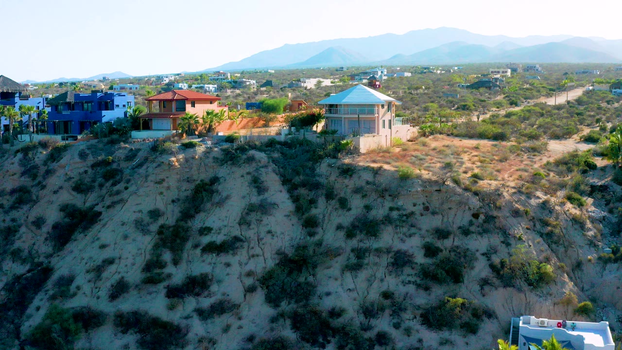 Aerial view of hillside homes, scrub terrain, dirt roads, and distant mountains.