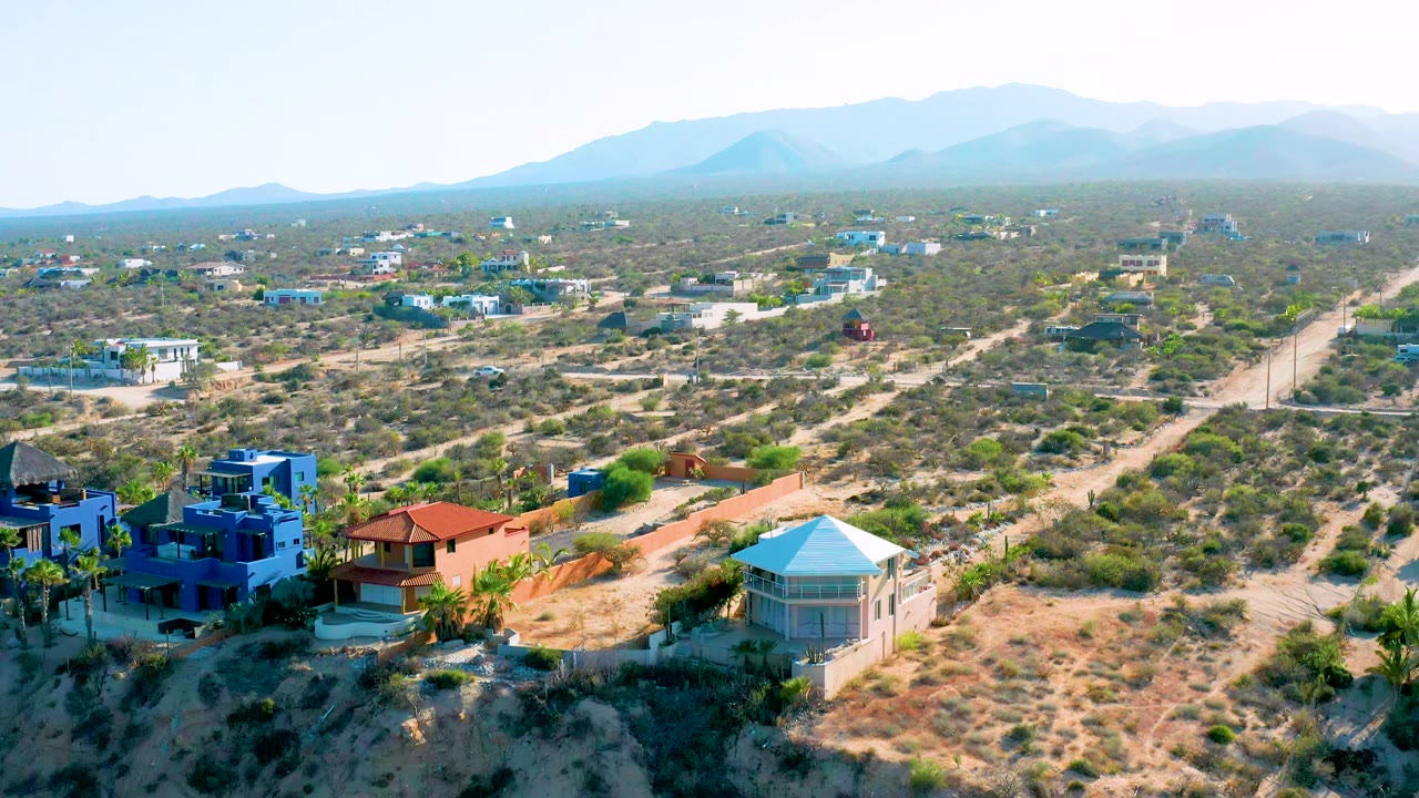 A slightly later view of El Sargento La Ventana, Mexico showing the same residential edge, sandy tracks crossing scrubland, low houses, hazy mountains, and no visible people.