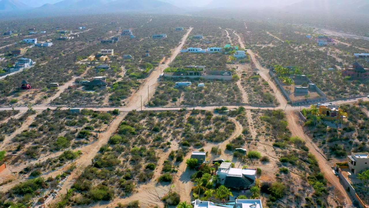 Aerial town view with parallel dirt roads, scrub, and distant mountains.