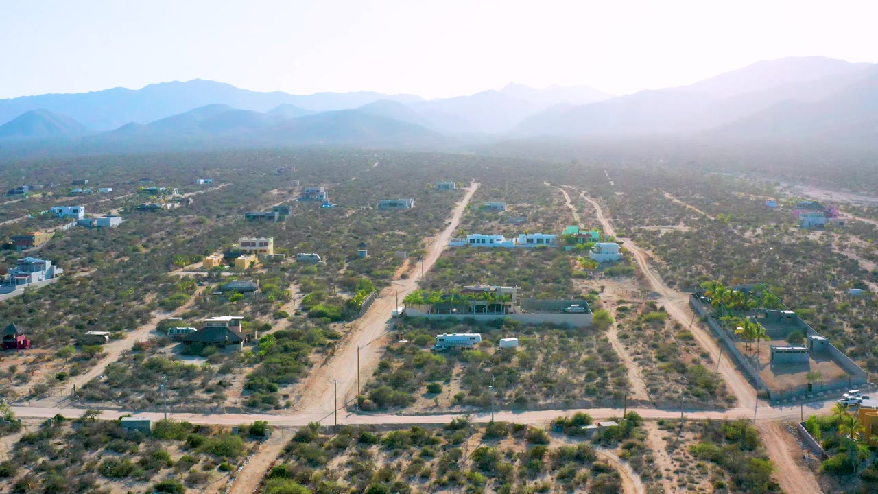 Aerial landscape with rural buildings, pale roads, desert vegetation, and mountains.