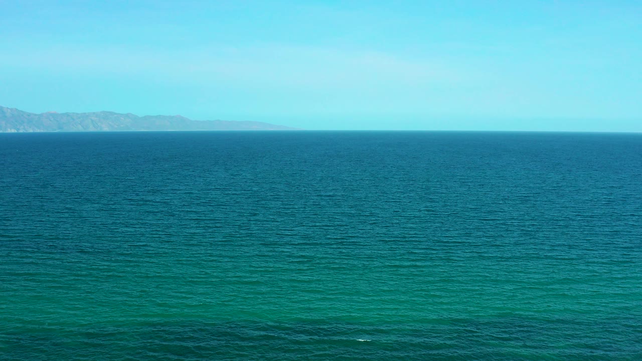 Blue-green ocean with distant mountains under a pale sky