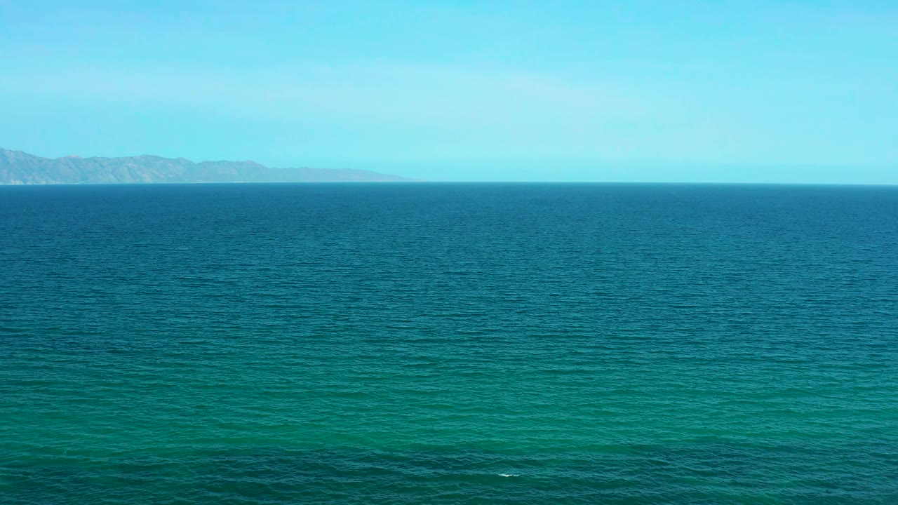 Blue-green water fills the foreground while a low mountain ridge sits across the horizon near El Sargento La Ventana, Mexico, with no visible people.