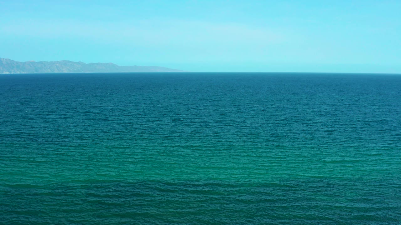 The ocean remains dominant while distant landforms appear at the left and center horizon near El Sargento La Ventana, Mexico, with no visible people.