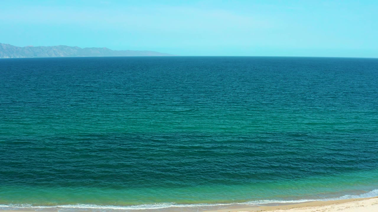 Open sea fills most of the frame with a straight horizon and faint coastal land beyond the water in El Sargento La Ventana, Mexico, with no visible people.