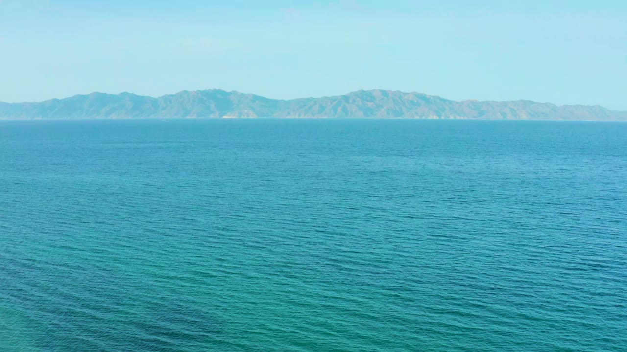 Wide view of rippling blue water at El Sargento La Ventana, Mexico, with a distant mountain range across the horizon and no visible people.
