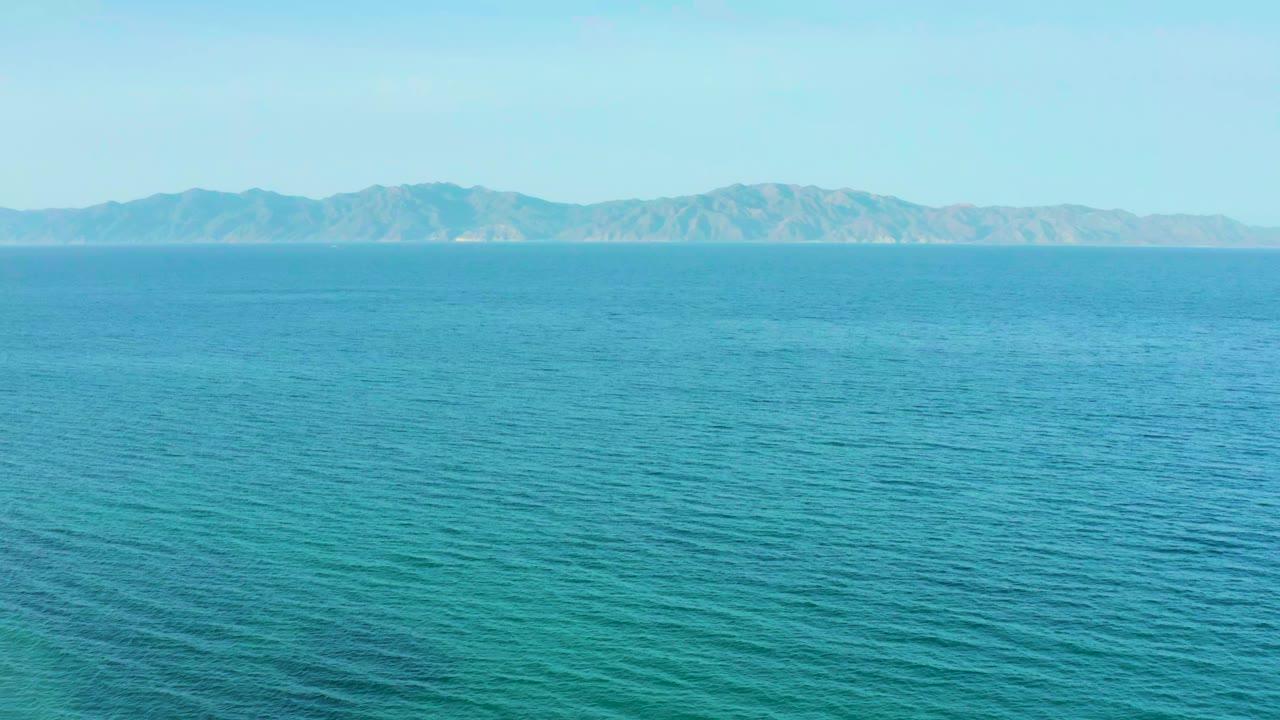 Turquoise water fills most of the frame at El Sargento La Ventana, Mexico, with hazy mountains on the horizon and no visible people.