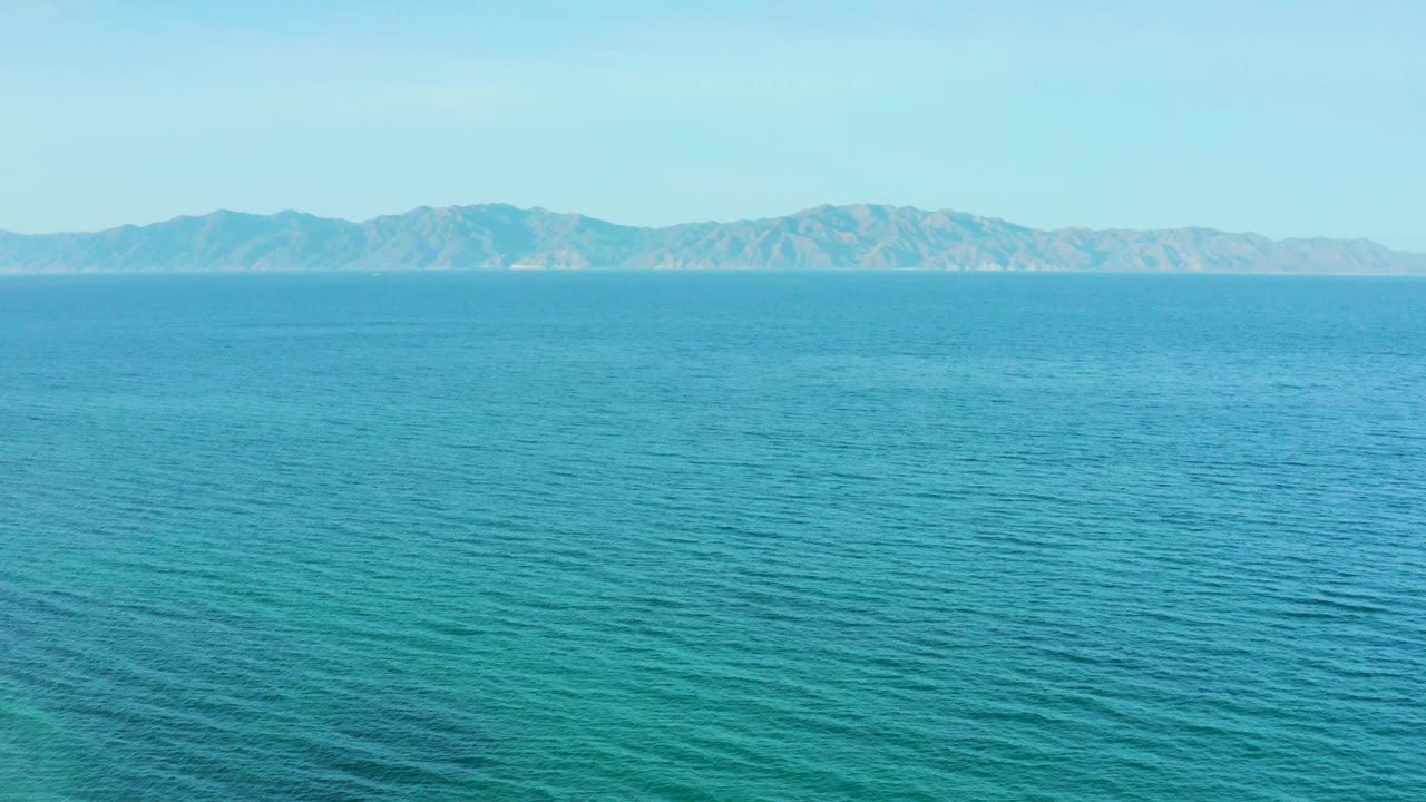 Open blue sea at El Sargento La Ventana, Mexico, stretches toward low mountain ridges beneath a clear sky, with no visible people.
