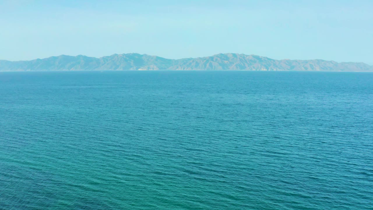 Turquoise sea stretches across the frame with a low mountain range on the horizon in El Sargento La Ventana, Mexico, and no visible people.