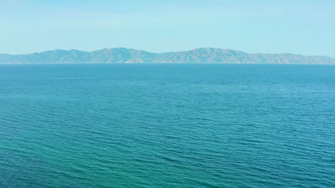 Open blue water fills most of the frame while rugged mountains remain small and steady along the background, with no visible people, buildings, or vessels.