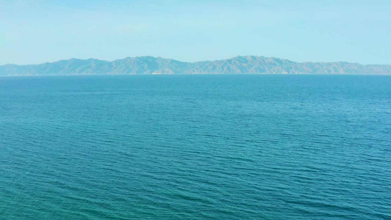 Blue-green ocean stretches across the frame toward hazy mountains on the horizon in El Sargento La Ventana, Mexico, with no visible people or vessels.