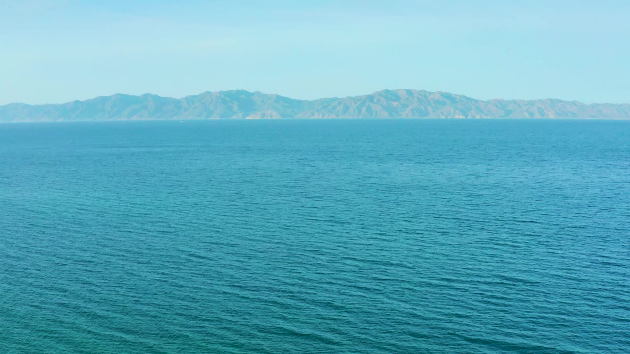 Open ocean fills the foreground and midground while the mountain range spans the background beneath a clear sky in El Sargento La Ventana, Mexico, with no visible people.