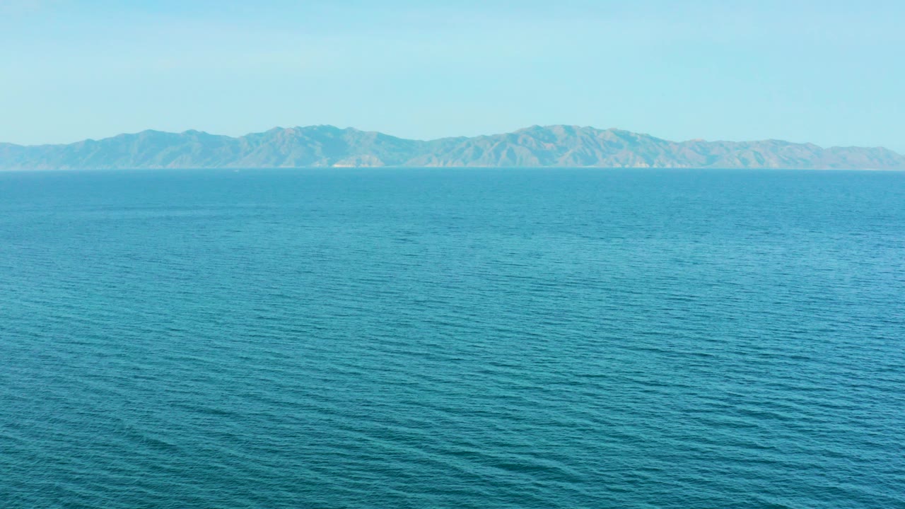 Opening frame of turquoise sea and distant mountain ridges in El Sargento La Ventana, Mexico, with no visible people.