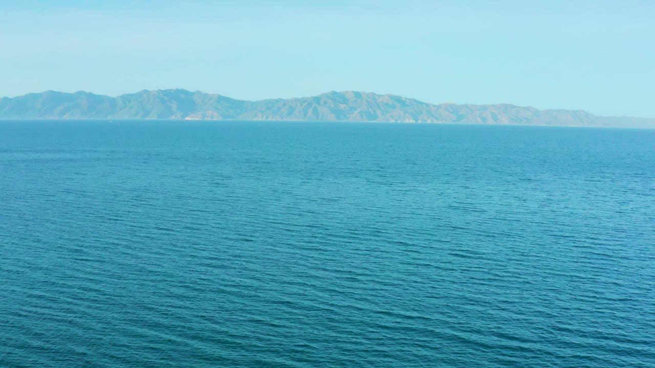 Third frame of El Sargento La Ventana, Mexico, showing calm blue water with fine surface texture and a centered distant mountain range under clear sky, with no visible people.