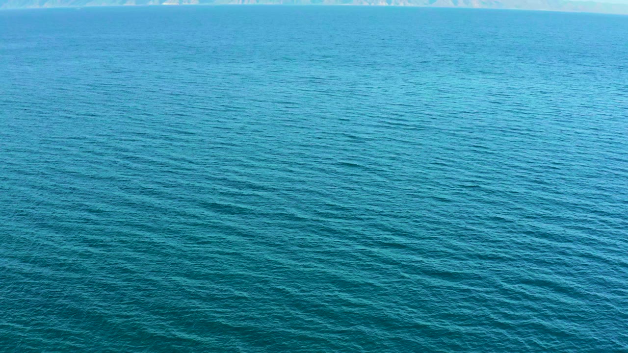 Elevated view over blue ocean water in El Sargento La Ventana, Mexico, with a faint pale land strip near the top edge and no visible people.