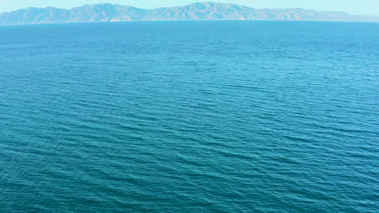 El Sargento La Ventana offshore frame showing calm blue water across most of the view, faint mountain ridges at the horizon, and no visible people.