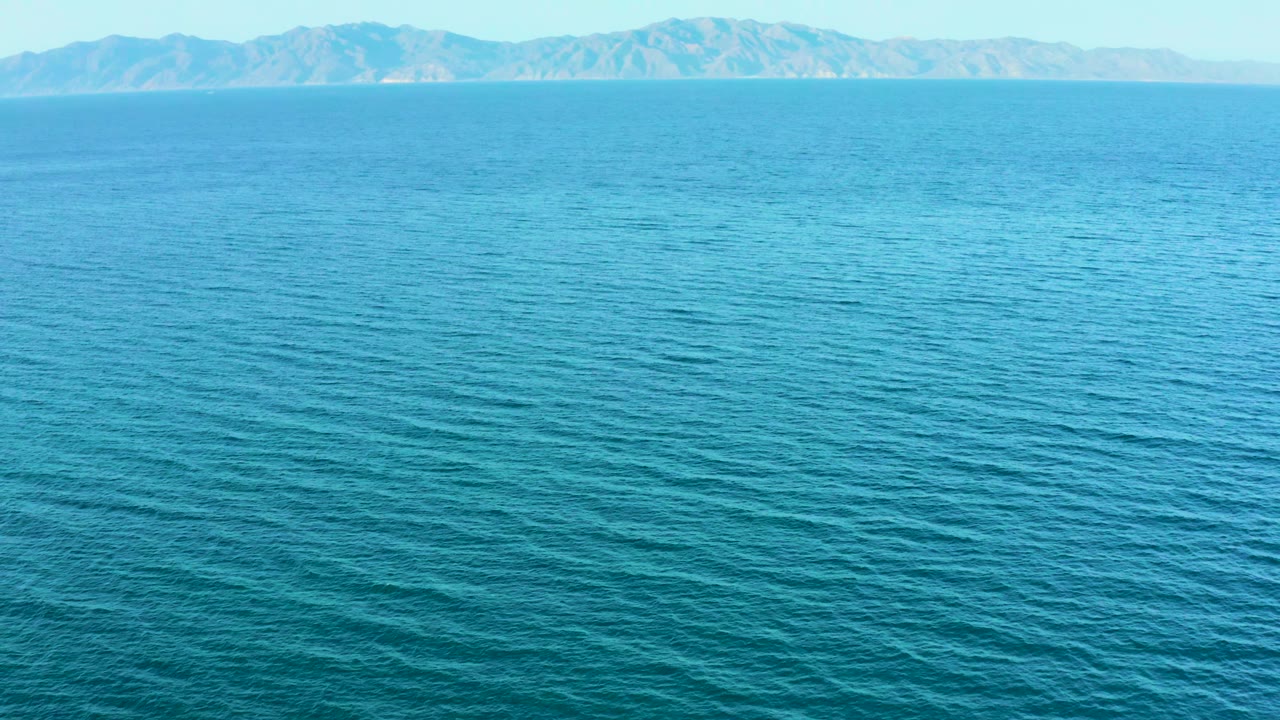 Open turquoise-blue water fills the frame in El Sargento La Ventana, Mexico, with rugged tan mountains stretching across the far background and no visible people.