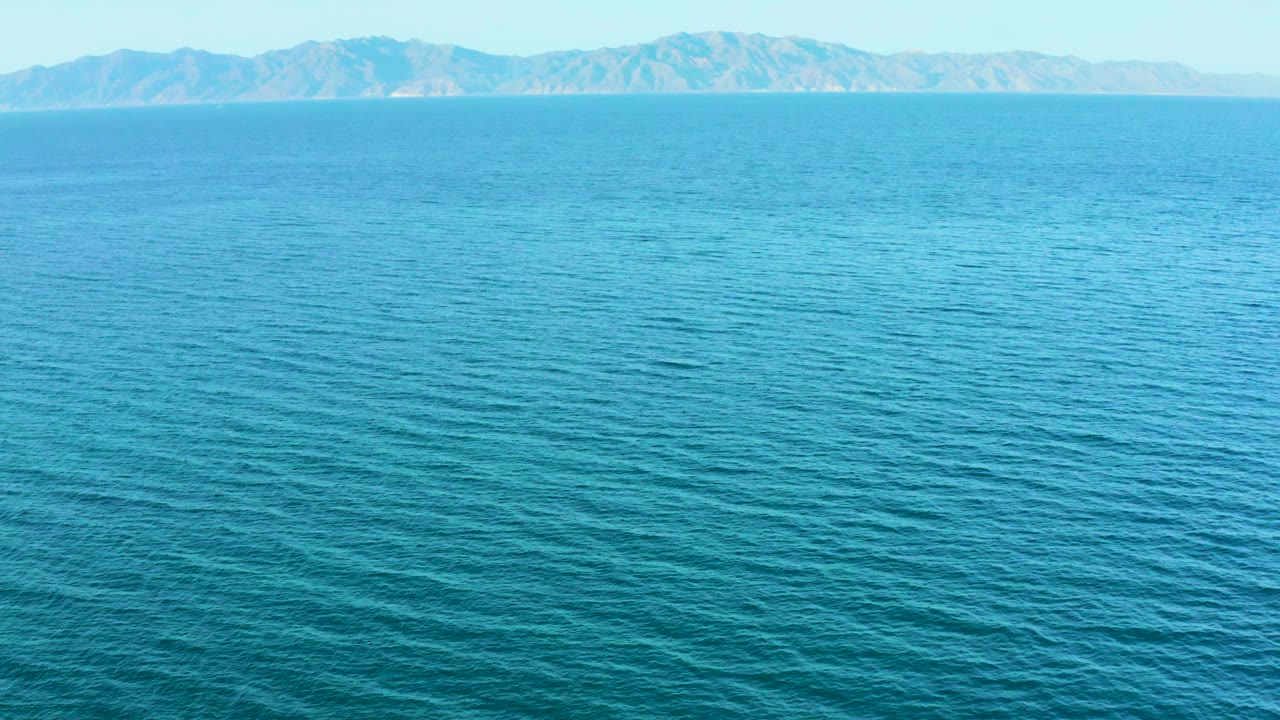 A bright blue ocean surface leads to a distant mountainous coastline in El Sargento La Ventana, Mexico, with clear sky above and no visible people.