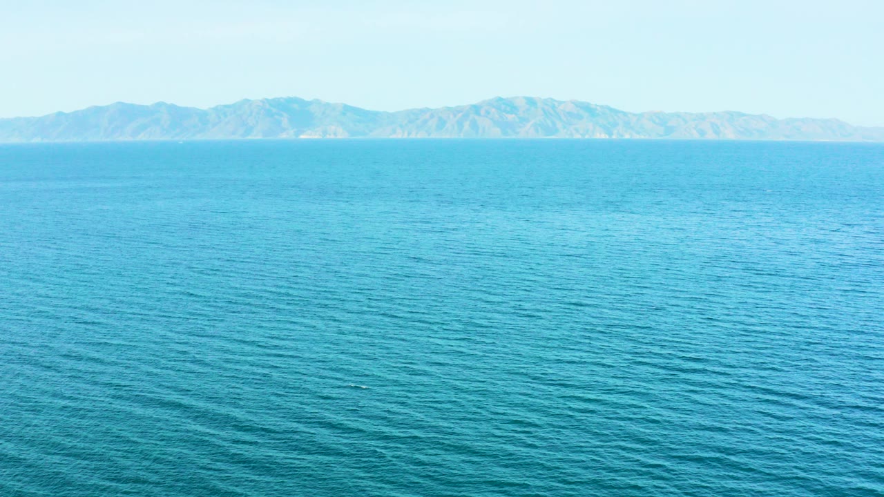 Wide blue ocean with distant mountains and pale sky