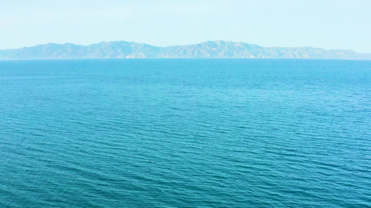 Blue-green sea fills most of the frame near El Sargento La Ventana, Mexico, with a low mountain coastline across the upper background and no visible people.