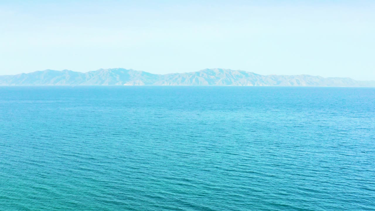 Opening frame of turquoise sea and a hazy mountain line in El Sargento La Ventana, Mexico, with no visible people.