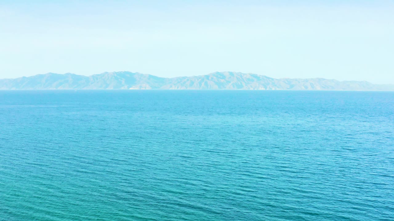 A bright sea view shows textured blue water below a low mountain range in El Sargento La Ventana, Mexico, with no visible people.