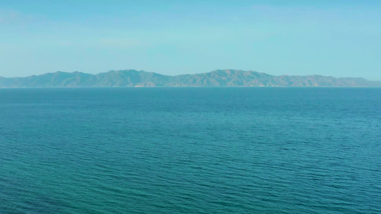 Early frame from El Sargento La Ventana, Mexico, with textured blue water in the foreground and the mountain range stretched across the upper horizon, with no visible people.