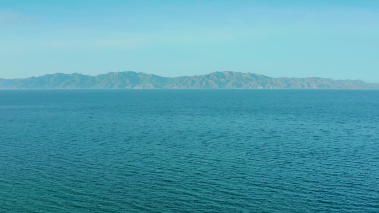 Wide coastal water view from El Sargento La Ventana, Mexico, showing fine ripples across aquamarine sea, hazy mountain shapes in the distance, and no visible people.