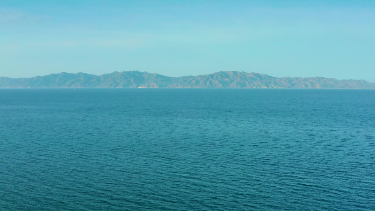 Wide blue sea with distant mountains and pale sky