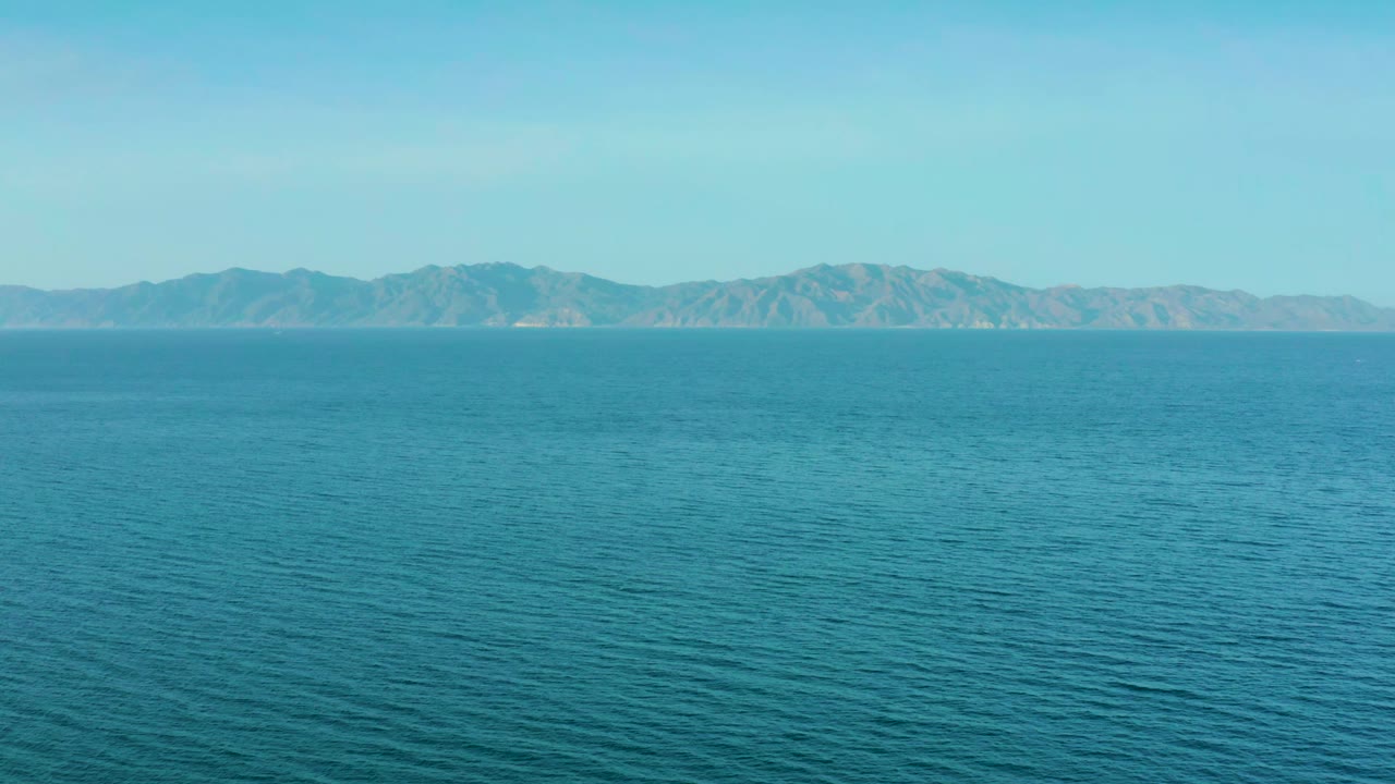Open turquoise water fills the lower frame while hazy mountains stretch across the horizon near El Sargento La Ventana, Mexico, with no visible people.