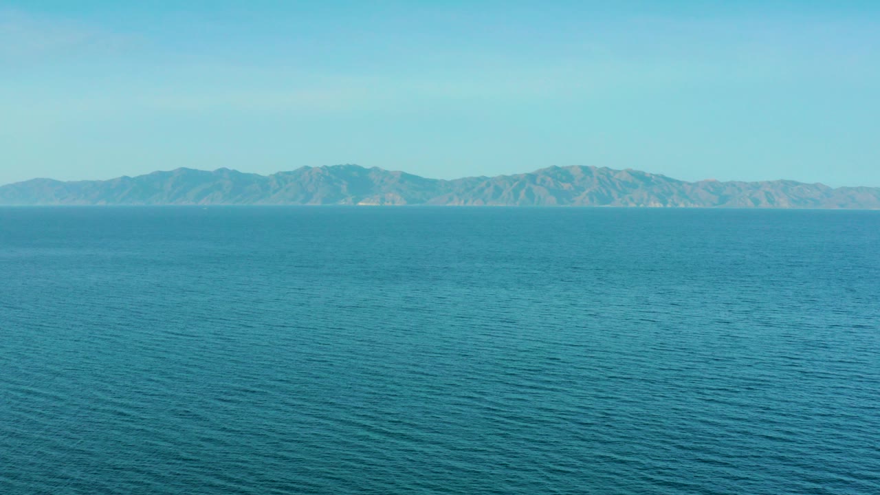 Blue ocean with distant mountains under a pale sky.