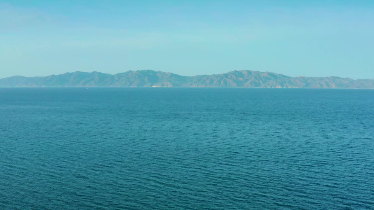 Blue sea fills most of the frame while the mountain ridge sits low on the horizon near El Sargento La Ventana, Mexico, with no visible people.