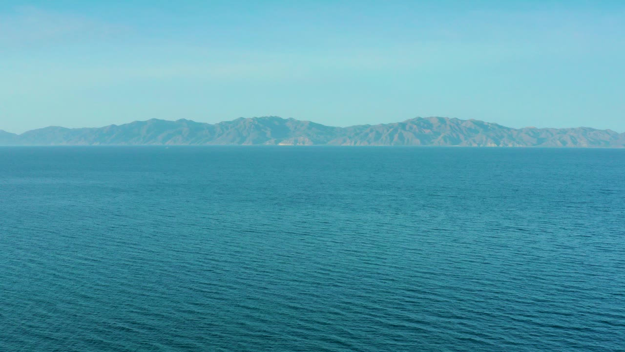 Opening frame of calm blue-green water facing distant mountains in El Sargento La Ventana, Mexico, with no visible people.