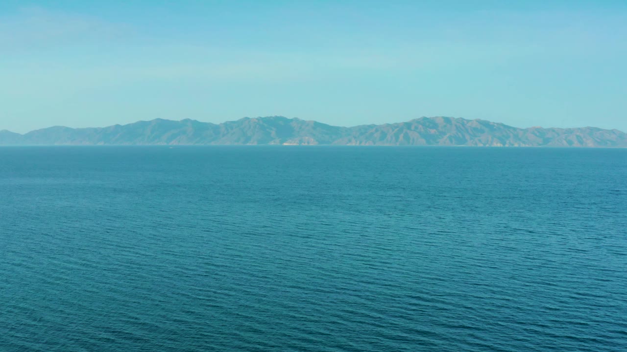 Mid-clip frame with blue-green water filling most of the view, hazy mountains across the horizon, and no visible people in El Sargento La Ventana, Mexico.