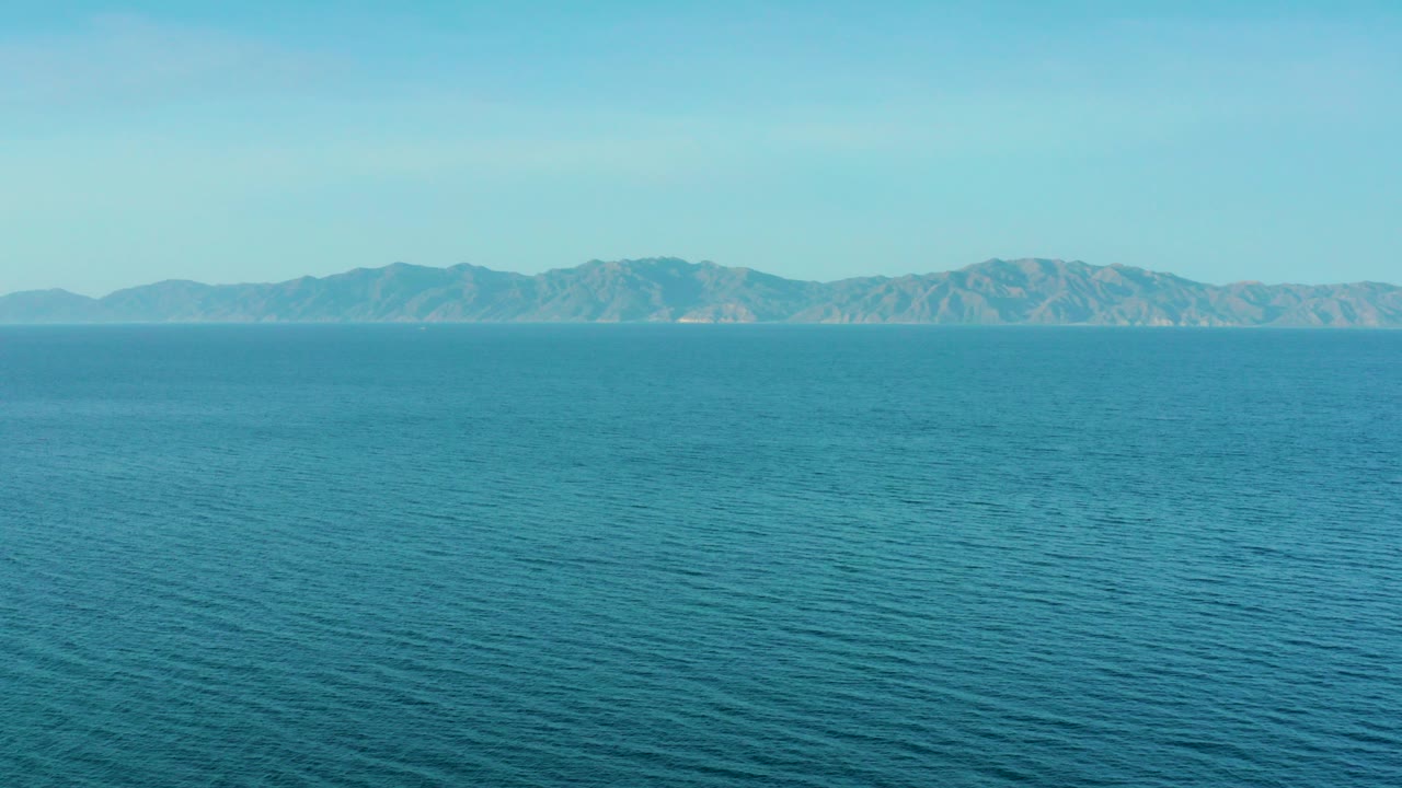 Opening frame of blue water stretching toward distant mountains near El Sargento La Ventana, Mexico, with clear sky and no visible people.